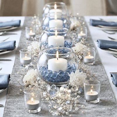 Wedding table centerpiece with candles, blue gems, and white flowers on a silver runner - thumbnail number 4