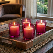 Four lit candles in pink holders on a wooden tray with a cozy armchair in the background - thumbnail number 8
