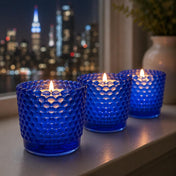 Blue hobnail glass votive candles glowing by city window at night - thumbnail number 7
