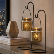 Two lit metallic gold mercury glass jars on black hanging stands beside a modern geometric vase - thumbnail number 6