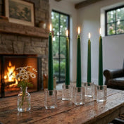 Lit green taper candles on wooden table beside glowing fireplace - thumbnail number 7