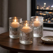 Three glass candle holders with glowing candles on wooden table by city window at night - thumbnail number 8