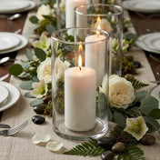 Lit white pillar candles in glass cylinder vases with roses and greenery on a table runner - thumbnail number 6