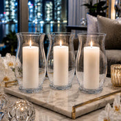 A lit white pillar candle burning inside a clear glass 10.5" Hurricane Vase on a dining tablescape - thumbnail number 8
