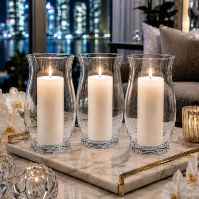 A lit white pillar candle burning inside a clear glass 10.5" Hurricane Vase on a dining tablescape - thumbnail number 8