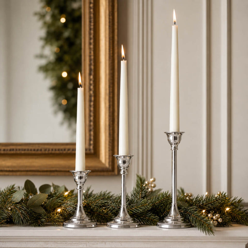 Three lit taper candles in silver holders on a mantle with evergreen garland - thumbnail number 8