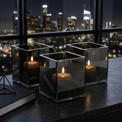 Modern square glass candle holders glowing by city window - thumbnail number 8