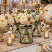 Floral arrangements in glass jars with metal handles on a wedding table with lit candles - thumbnail number 3