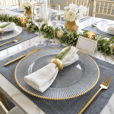 Glass charger with gold rim and napkin on a blue placemat at a formal dinner table - thumbnail number 4