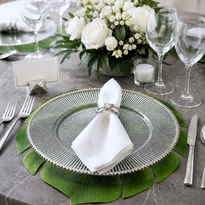 Glass charger with silver rim and napkin on a leaf placemat at a formal dinner table - thumbnail number 4