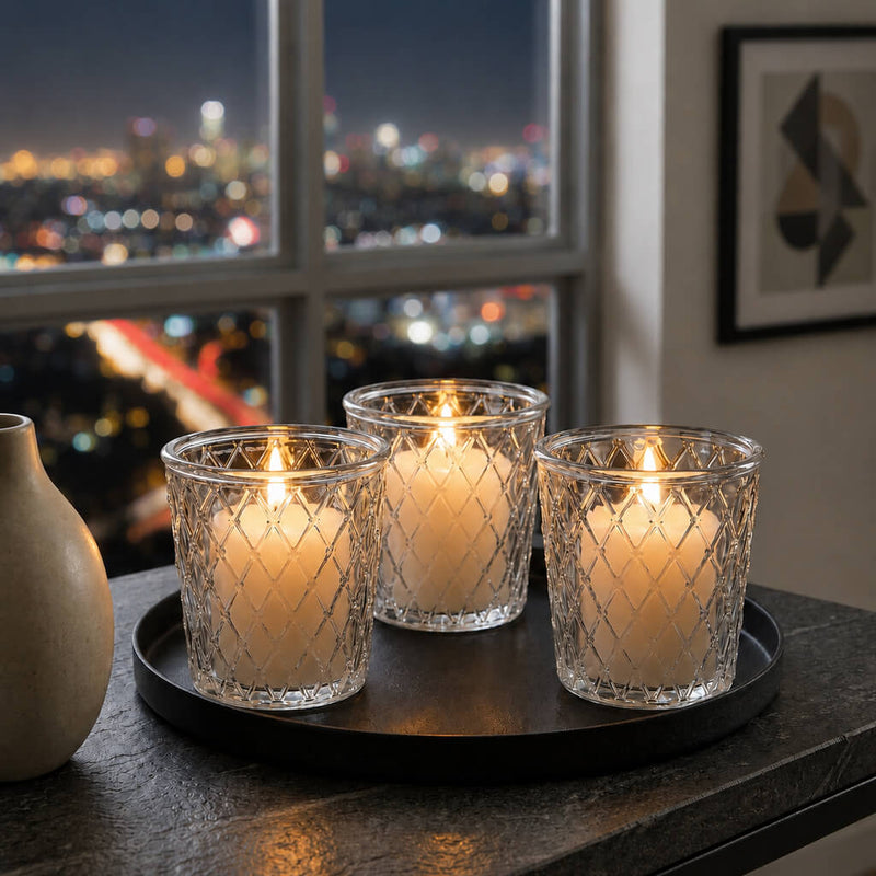 Three clear Tipper Vase & Candle Holders casting a warm glow against a nighttime city backdrop - thumbnail number 7