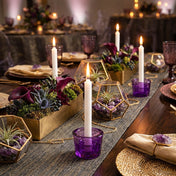Lit white taper candles in purple glass holders on a decorated event table - thumbnail number 7