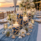 Glass cylinder vases with lit candles, filled with navy blue and gold pearls on a seaside table - thumbnail number 2