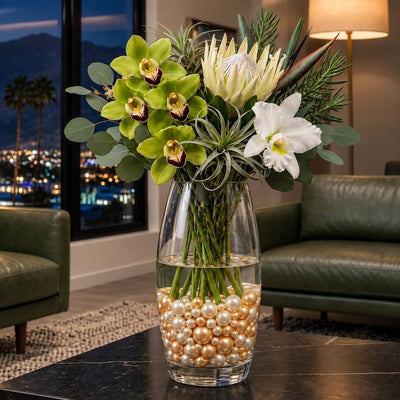 A tall glass vase with flowers sitting on a table, filled with off-white and gold pearls - thumbnail number 9
