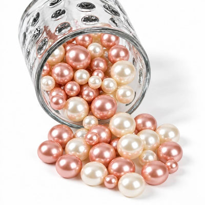 Rose gold and off-white pearl beads spilling from a textured glass jar onto a white background - thumbnail number 1