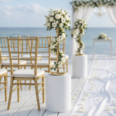 Gold metal flower stand decorated with white florals on a white pedestal at a beach wedding - thumbnail number 5