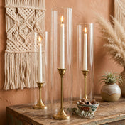 Lit white taper candles in gold holders with a chimney glass candle shade on a rustic wood table - thumbnail number 8