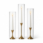 Lit white taper candles in gold holders with chimney glass candle shade cylinders - thumbnail number 2