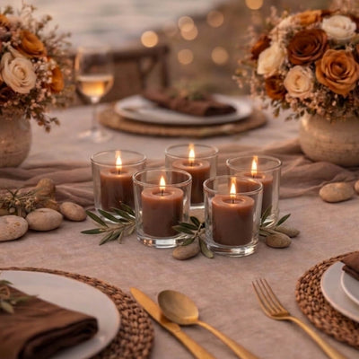 Five lit brown votive candles in glass holders on a table set with flowers and place settings - thumbnail number 5
