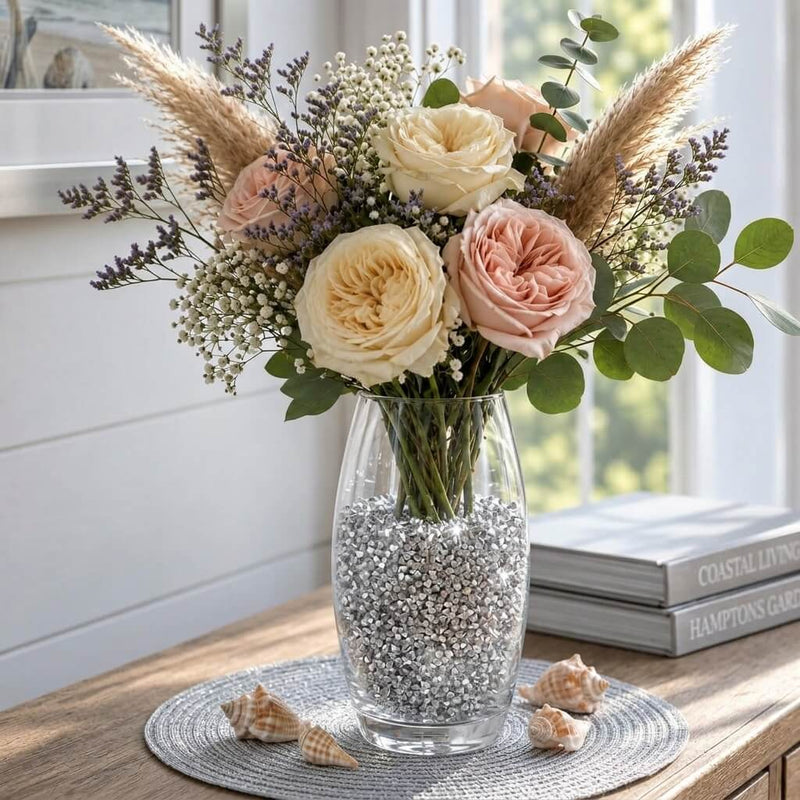 Floral bouquet in a clear glass vase filled with sparkling silver faux diamond gems on a table - thumbnail number 6