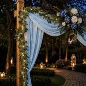 Eucalyptus garland with warm white LED lights wrapped around an outdoor wedding arch at dusk - thumbnail number 4