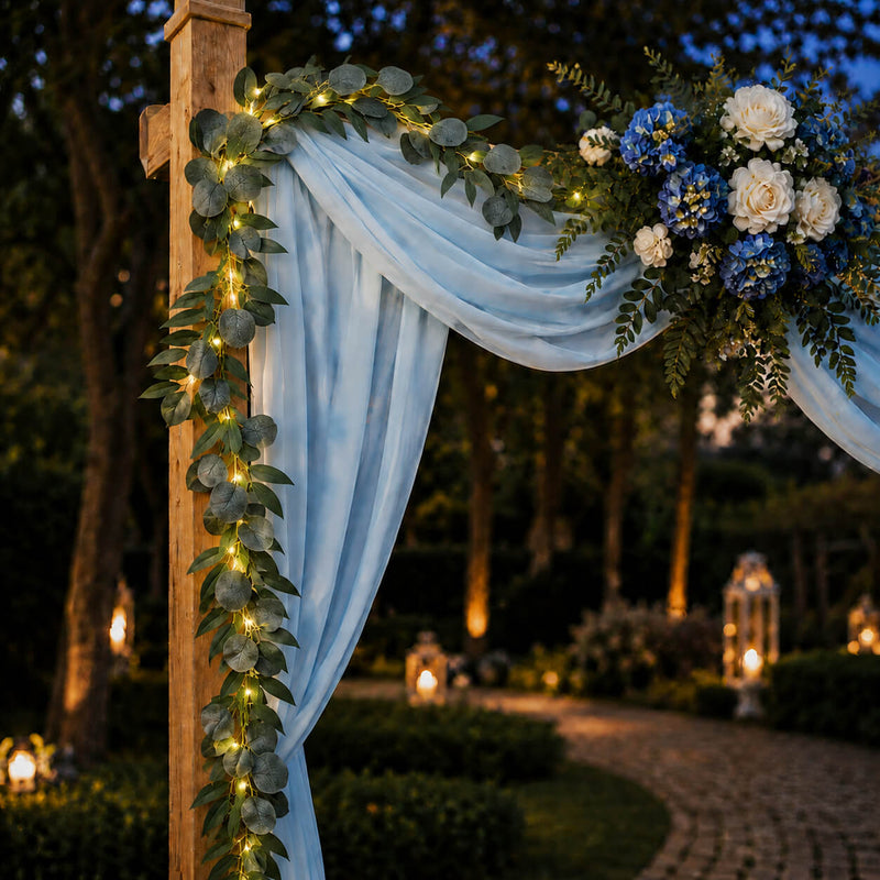 Eucalyptus garland with warm white LED lights wrapped around an outdoor wedding arch at dusk - thumbnail number 4