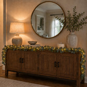 Eucalyptus garland with warm white LED lights draped over a wooden credenza under a round mirror - thumbnail number 8