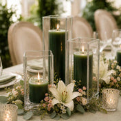 Three lit dark green candle and square holder sets on a table centerpiece with white lilies - thumbnail number 3