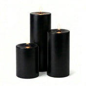 Three lit black pillar candles in assorted heights on a white background - thumbnail number 2