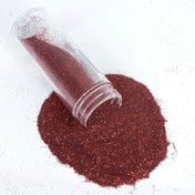 Clear tube spilling sparkling burgundy glitter onto a white surface. - thumbnail number 1