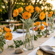 Orange poppy flower sprays in a tall glass vase on a rustic outdoor table setup - thumbnail number 3