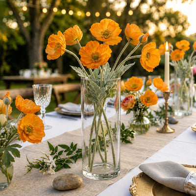 Orange poppy flower sprays in a tall glass vase on a rustic outdoor table setup - thumbnail number 3
