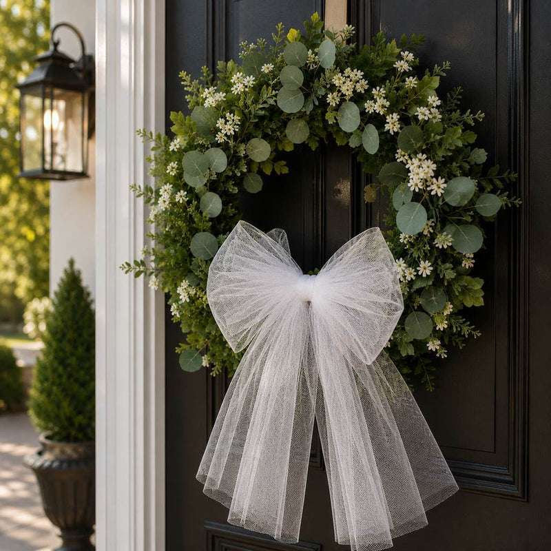 Greenery and white flower wreath with a large sheer white bow on a black door - thumbnail number 10