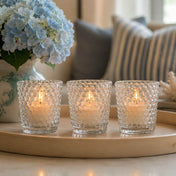 Three lit clear hobnail glass votive holders on a tray beside blue hydrangeas and striped pillows - thumbnail number 7