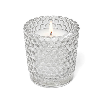 A lit white candle inside a clear hobnail glass votive holder on a solid white background - thumbnail number 3
