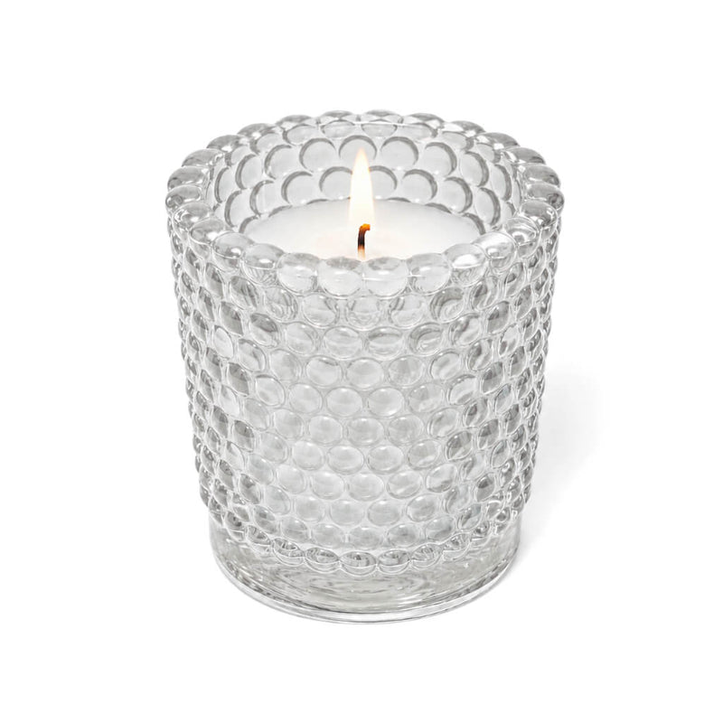 A lit white candle inside a clear hobnail glass votive holder on a solid white background - thumbnail number 3