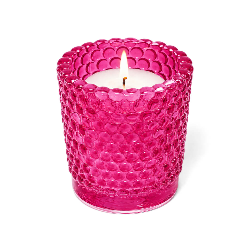 Pink hobnail glass votive holder with lit candle on white background