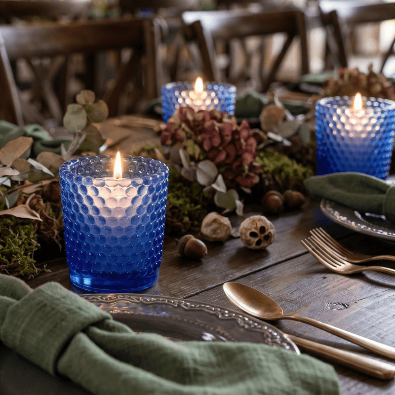 Blue glass hobnail votive holders with glowing candles on rustic floral dining table - thumbnail number 5