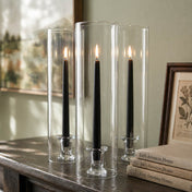 Lit black taper candles inside tall glass cylinders on wood table - thumbnail number 7