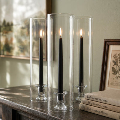 Lit black taper candles inside tall glass cylinders on wood table - thumbnail number 7