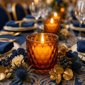 Decorative table setting with amber candles, blue napkins, and floral arrangements.