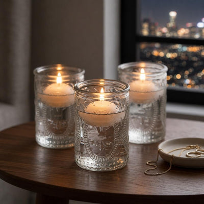 Three glass candle holders with glowing candles on wooden table by city window at night - thumbnail number 8