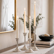 Four lit white taper candles in silver holders on a table with eucalyptus - thumbnail number 7