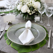 Glass charger with silver rim and napkin on a leaf placemat at a formal dinner table - thumbnail number 4