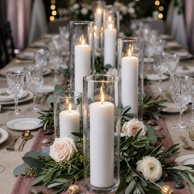 Lit white pillar candles in tall glass cylinder vases on a floral wedding table runner - thumbnail number 6