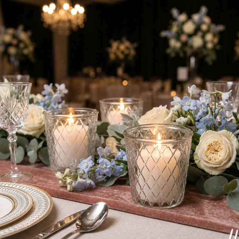 Lit white candles in tipper glass votive holders with blue and white flowers on a pink runner - thumbnail number 5