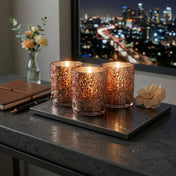 Rose gold mercury candle holders glowing beside window with city lights at night - thumbnail number 6