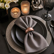 A rose gold napkin ring holding a folded grey napkin on a matte black plate - thumbnail number 9