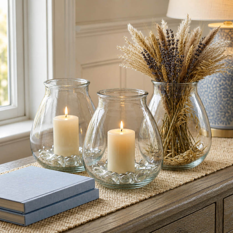 Two white pillar candles in glass jars with stones next to a floral vase - thumbnail number 9