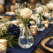 4.5" teardrop glass bottle with a white rose and greenery set on a blue table - thumbnail number 4